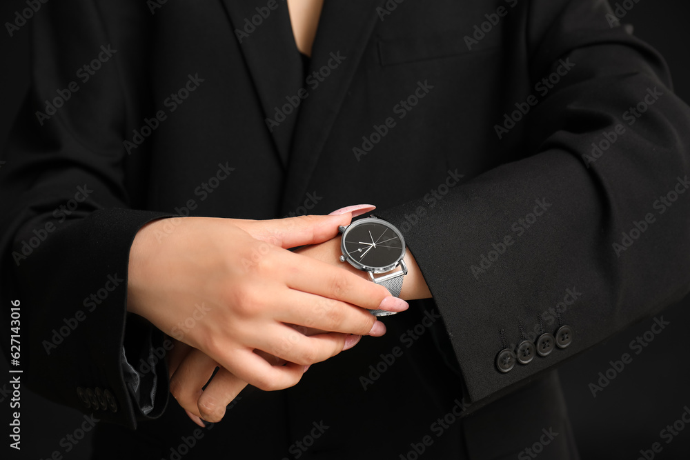 Young woman with wristwatch on black background