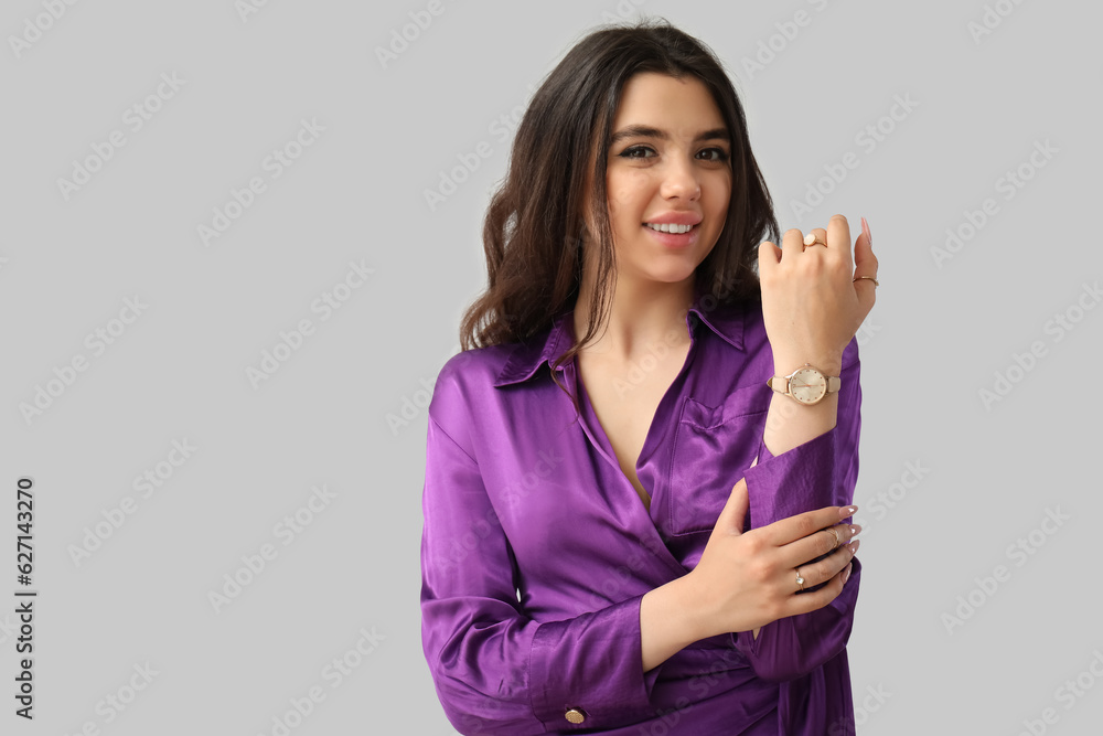 Elegant beautiful young woman with wristwatch on grey background