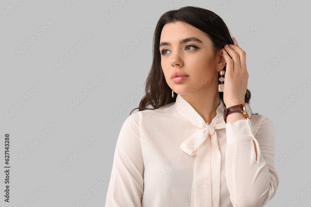 Elegant beautiful young woman with wristwatch on grey background