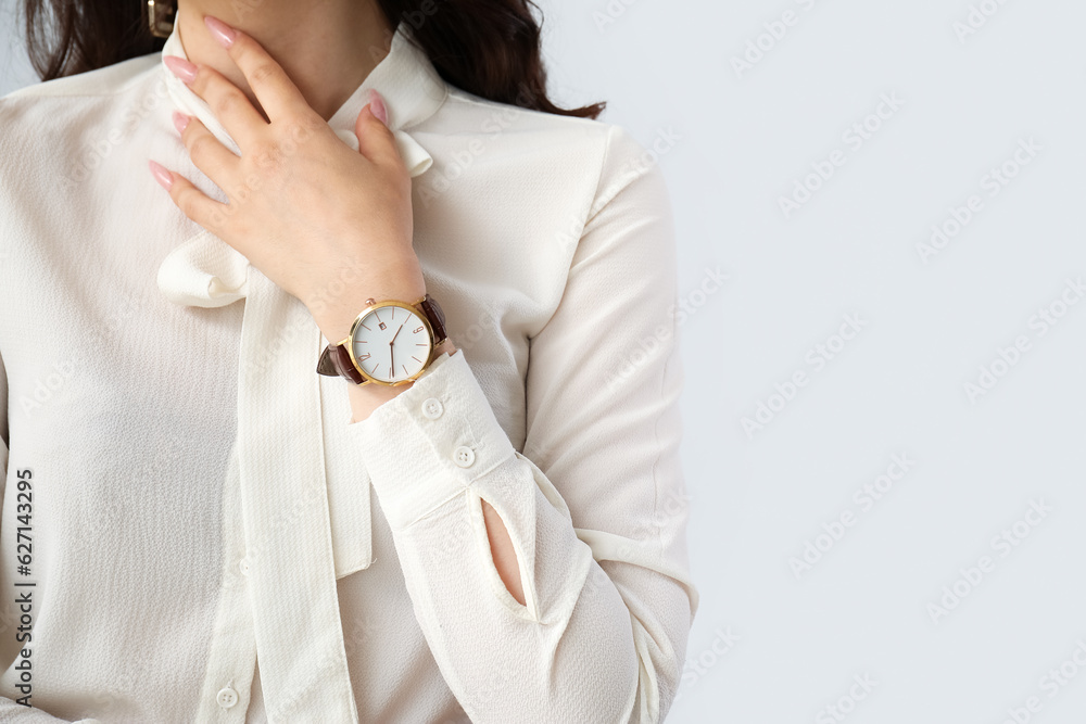 Elegant young woman with wristwatch on grey background