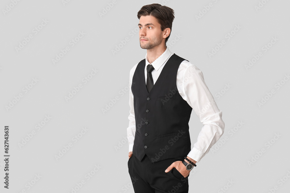 Handsome young businessman with wristwatch on grey background