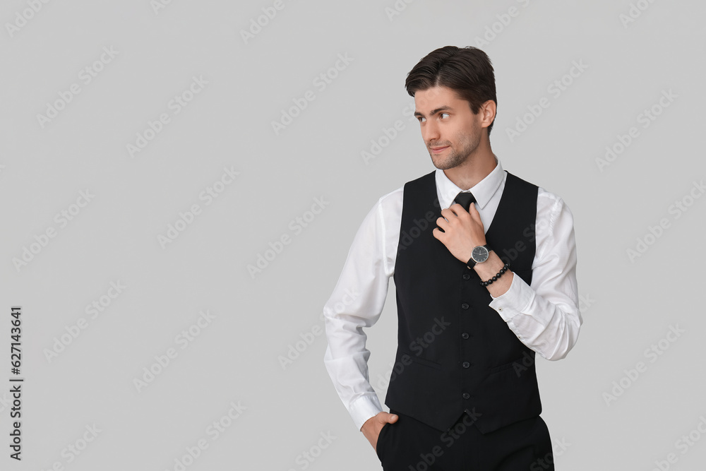 Handsome young businessman with wristwatch on grey background