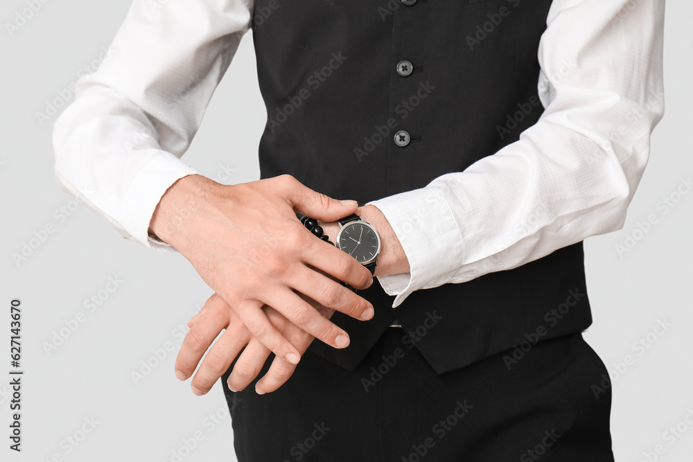 Stylish young businessman with wristwatch on grey background, closeup