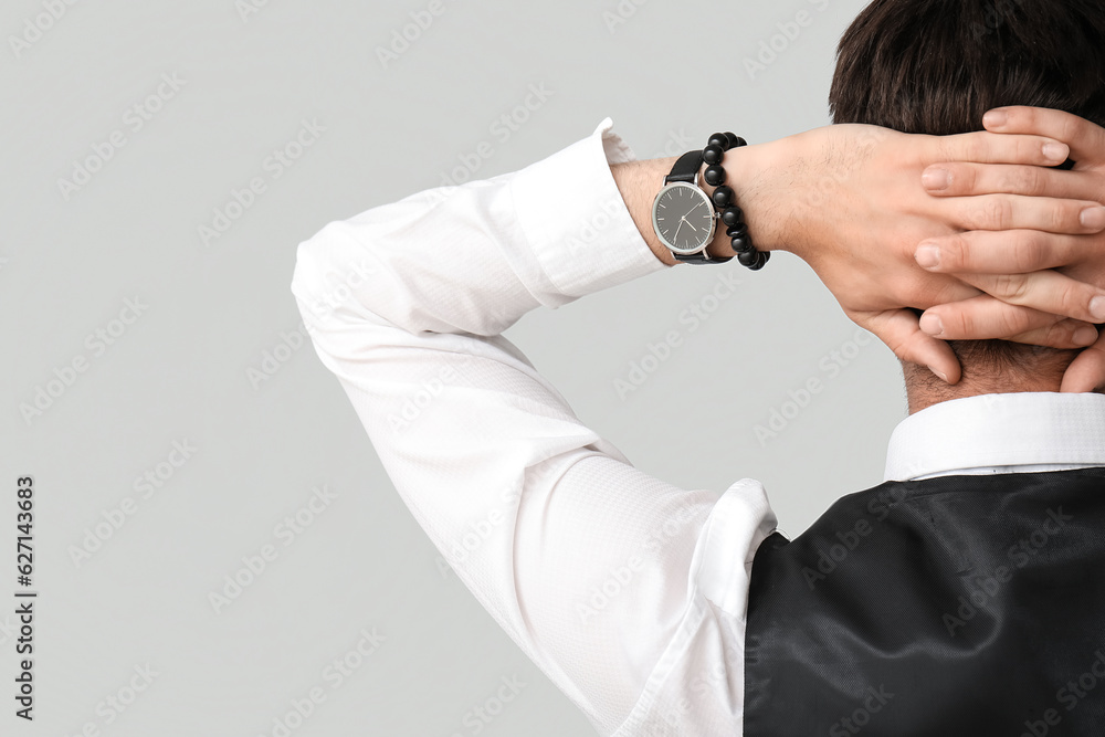 Stylish young businessman with wristwatch on grey background, back view