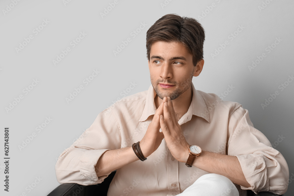 Handsome stylish young man with wristwatch sitting on armchair in room