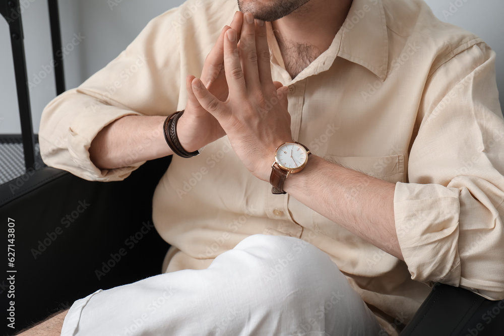 Handsome stylish young man with wristwatch sitting on armchair in room