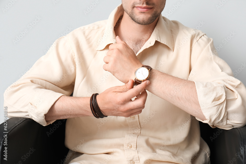 Handsome stylish young man with wristwatch sitting on armchair in room