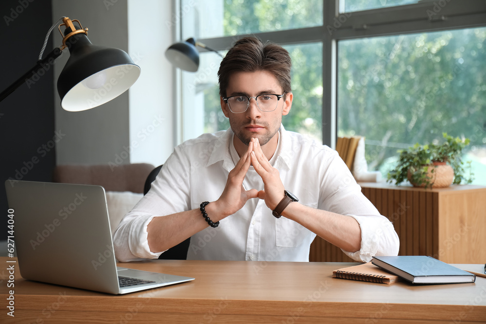 Stylish young man with wristwatch and eyeglasses working on laptop in office