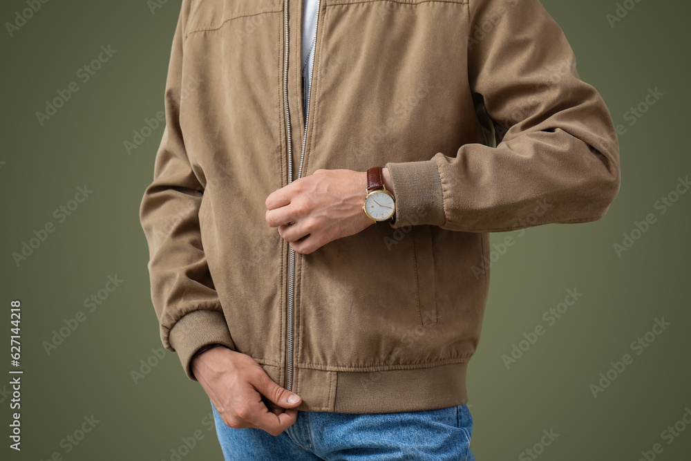 Stylish young handsome man with wristwatch zipping jacket on olive background