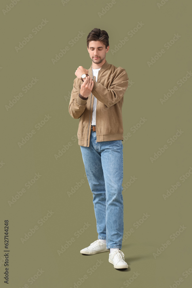 Young man with wristwatch in stylish jacket on olive background