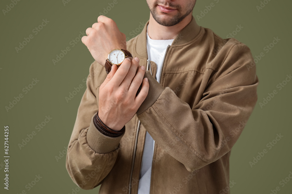 Young man with wristwatch in stylish jacket on olive background