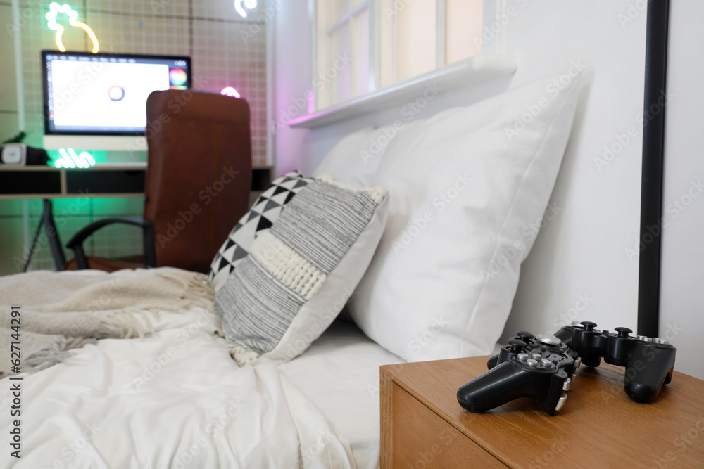 Interior of childrens bedroom with cozy bed and game pads on bedside table