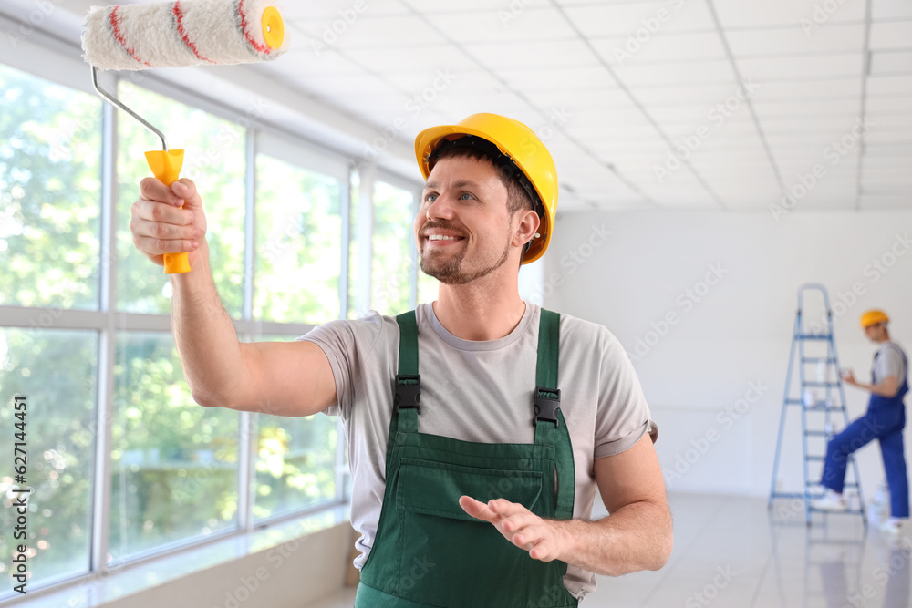 Male builder with paint roller in room