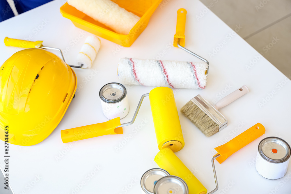 Builders hardhat with paint cans and rollers on table, closeup