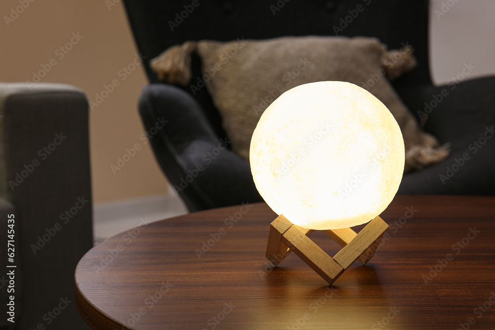 Glowing lamp in shape of moon on wooden table in living room, closeup