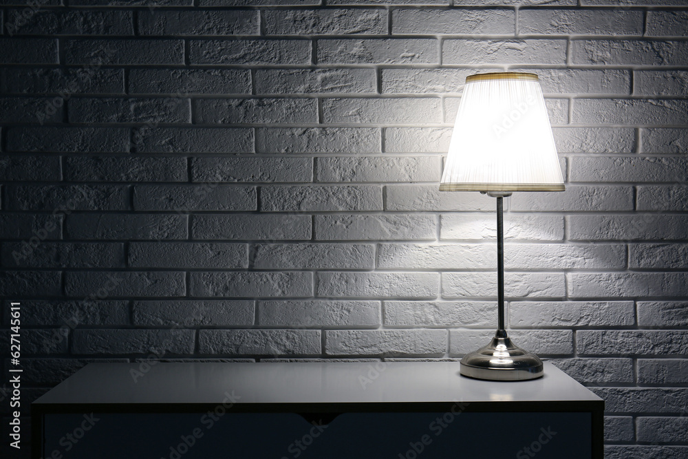 Glowing lamp on table near white brick wall in dark room