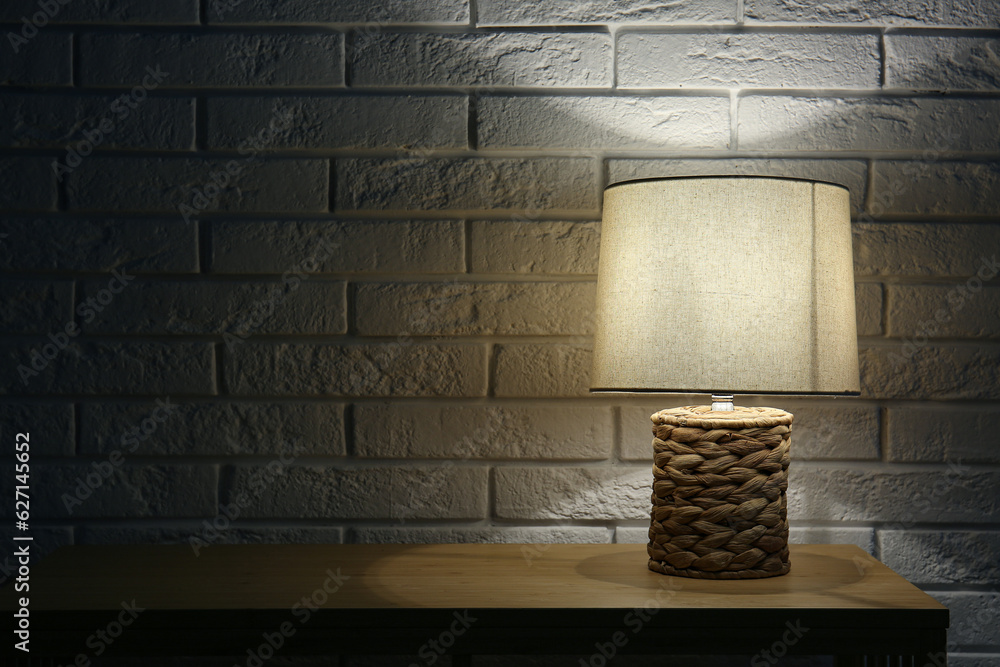 Glowing lamp on wooden table near white brick wall in dark room