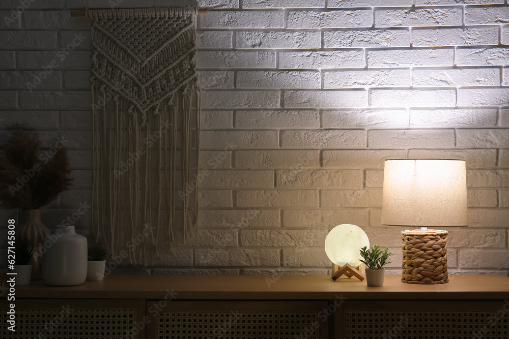 Different glowing lamps and houseplant on wooden table in dark room