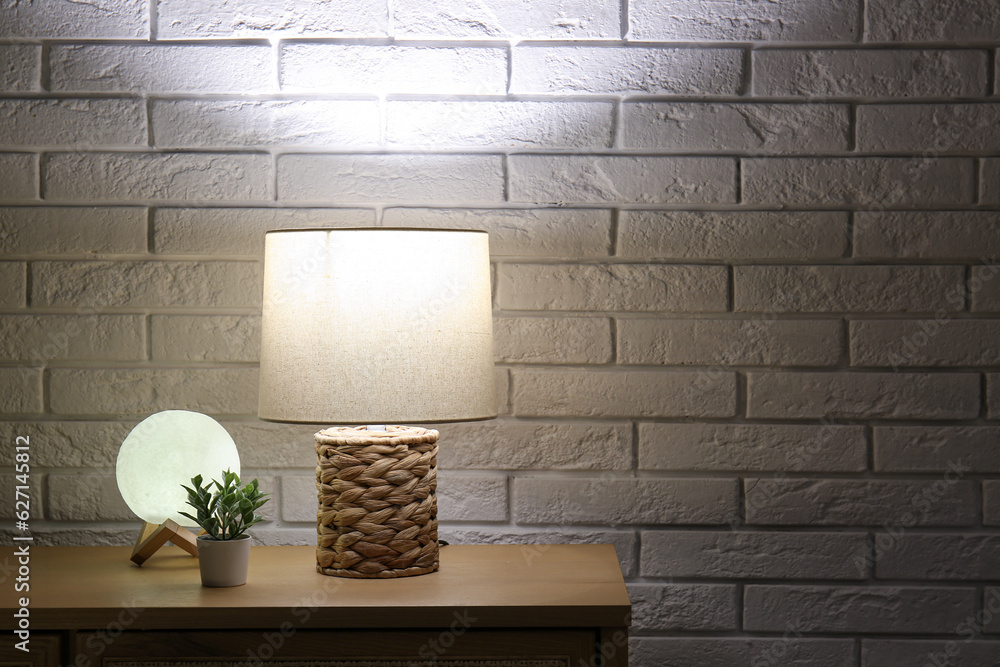 Different glowing lamps and houseplant on wooden table in dark room