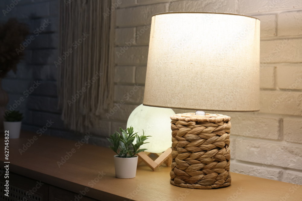 Different glowing lamps and houseplant on wooden table in dark room