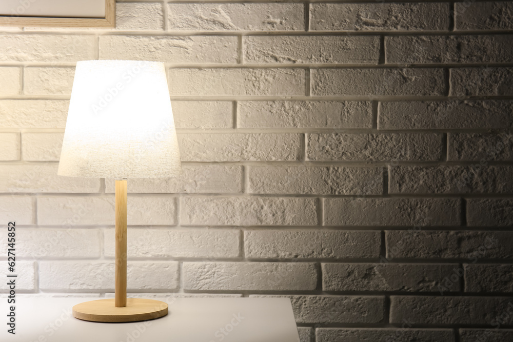 Glowing lamp on table near white brick wall in dark room