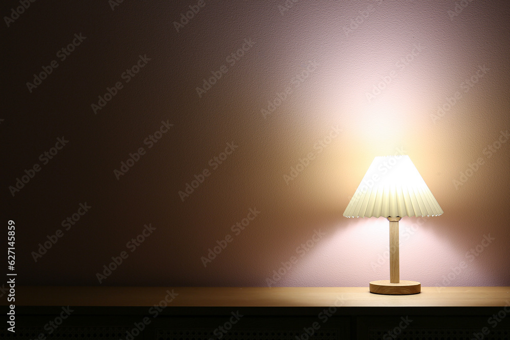 Glowing lamp on wooden table near beige wall in dark room