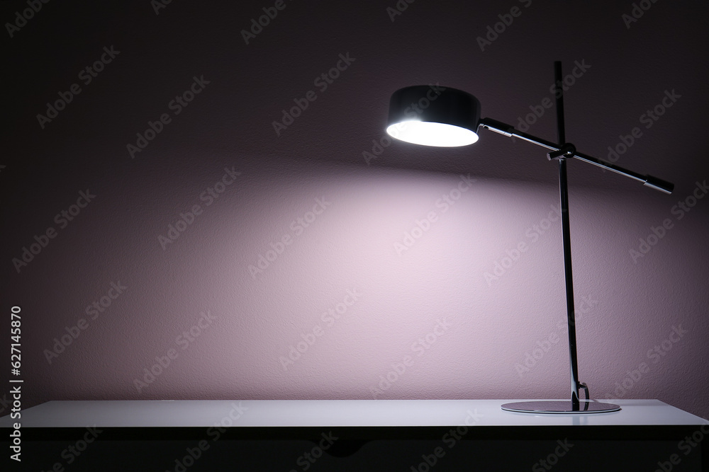 Glowing lamp on table near beige wall in dark room