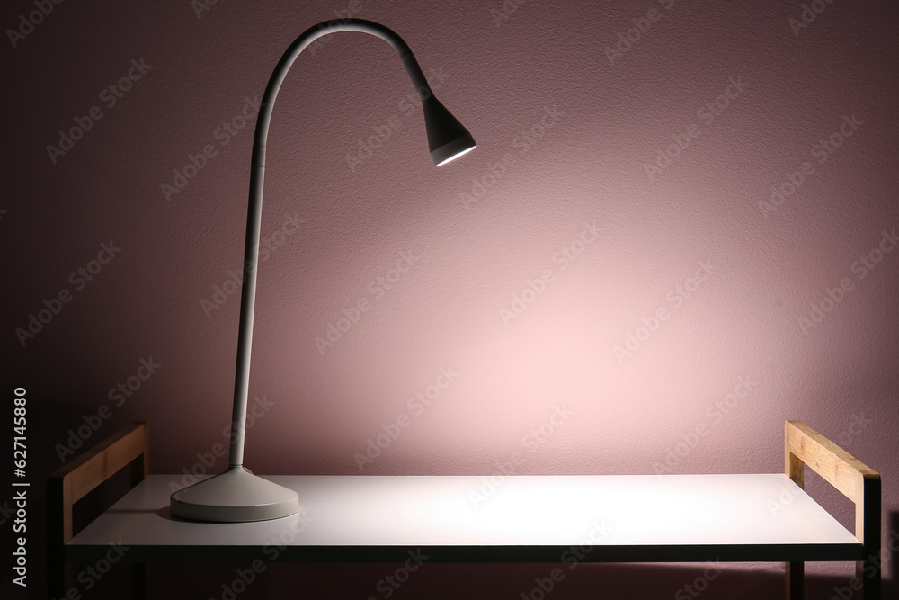 Glowing lamp on shelving unit near beige wall in dark room