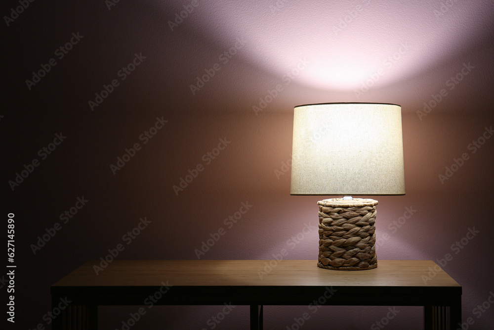 Glowing lamp on wooden table near beige wall in dark room