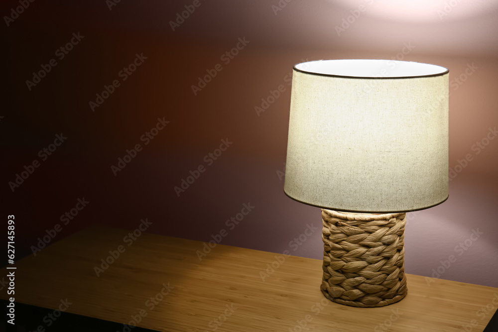 Glowing lamp on wooden table near beige wall in dark room