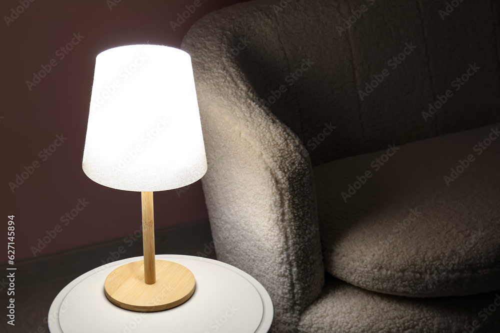 Glowing lamp on wooden table near sofa in dark room