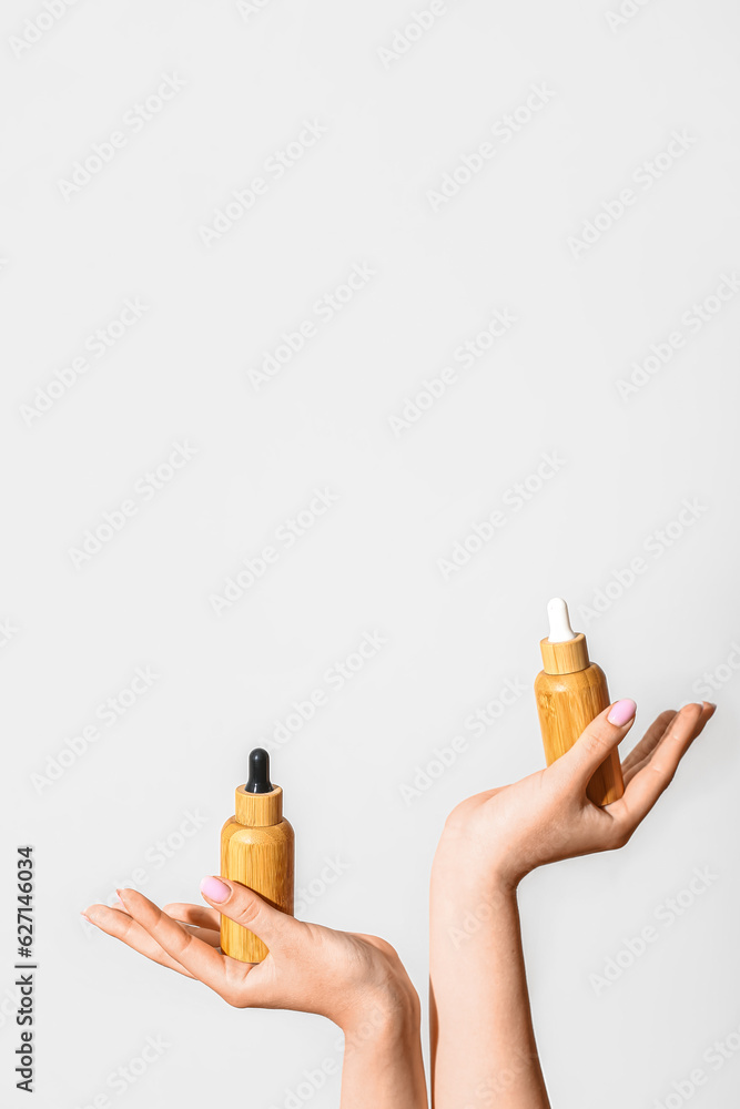 Hands of woman with bottles of cosmetic oil on light background