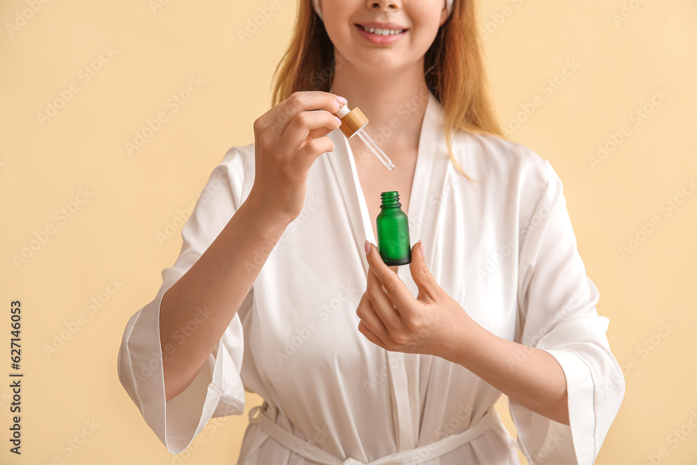 Pretty young woman with cosmetic oil on beige background