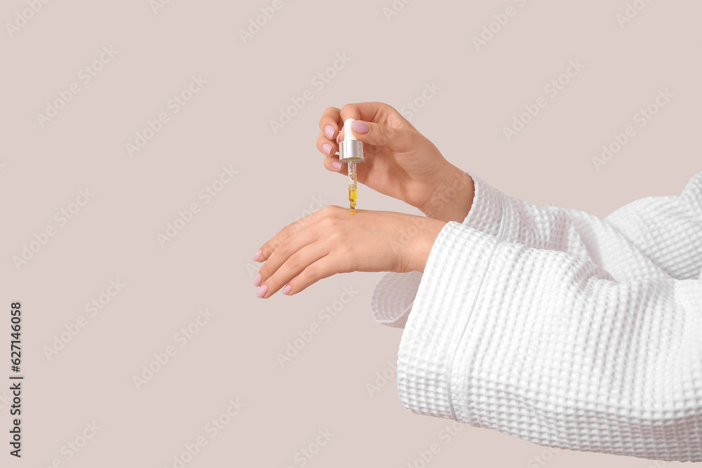 Hands of woman with cosmetic oil on light background