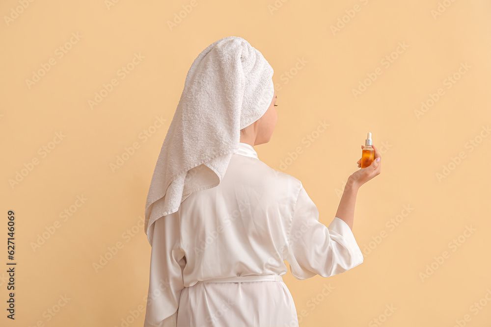 Pretty young woman with cosmetic oil on beige background