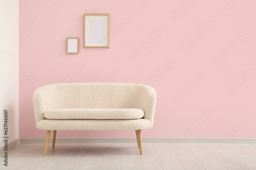 Cozy white sofa and blank frames near pink wall