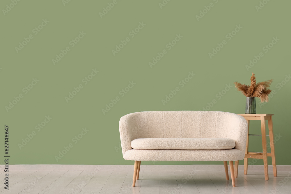 White sofa and vase with pampas grass on table near green wall