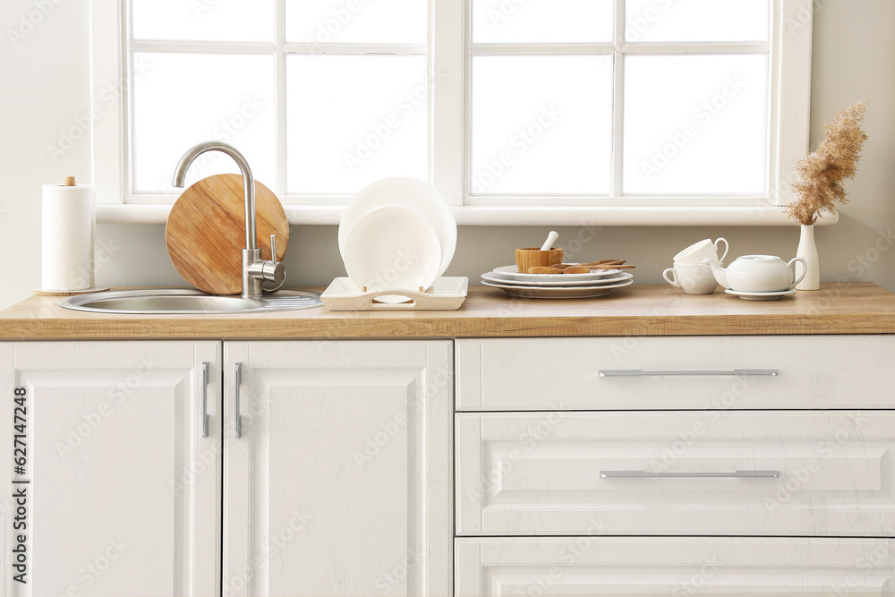 Kitchen counter with sink, plate rack and clean dishes near window