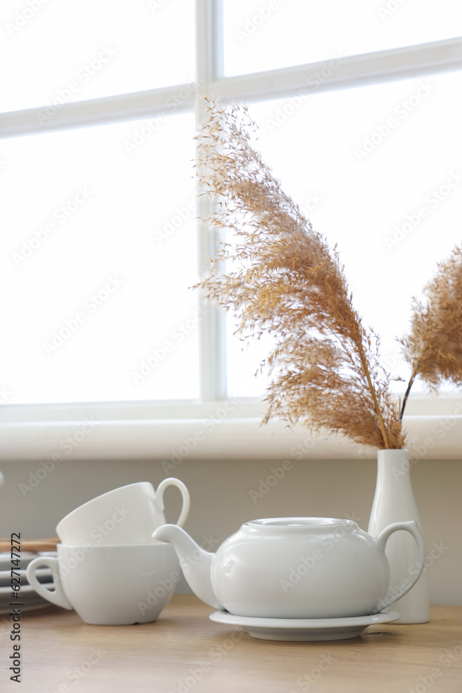 Teapot, cups and vase with pampas grass on wooden countertop, closeup