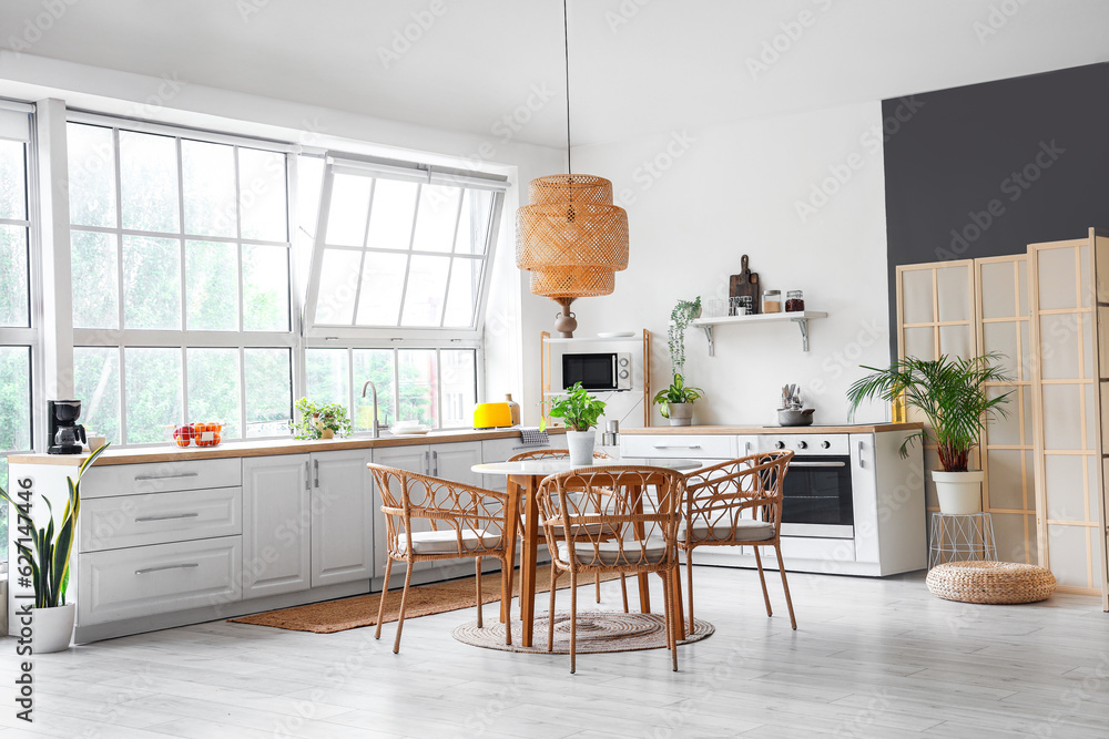 Interior of light kitchen with white counters, dining table and big window