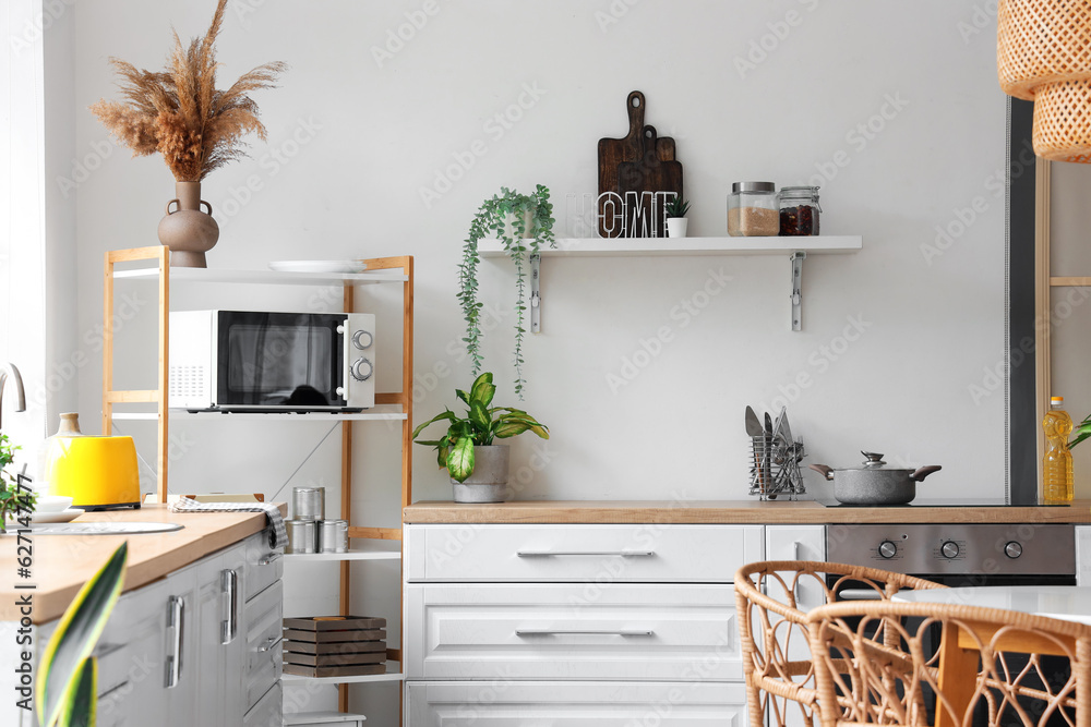 Interior of modern kitchen with white counters and microwave oven on shelving unit