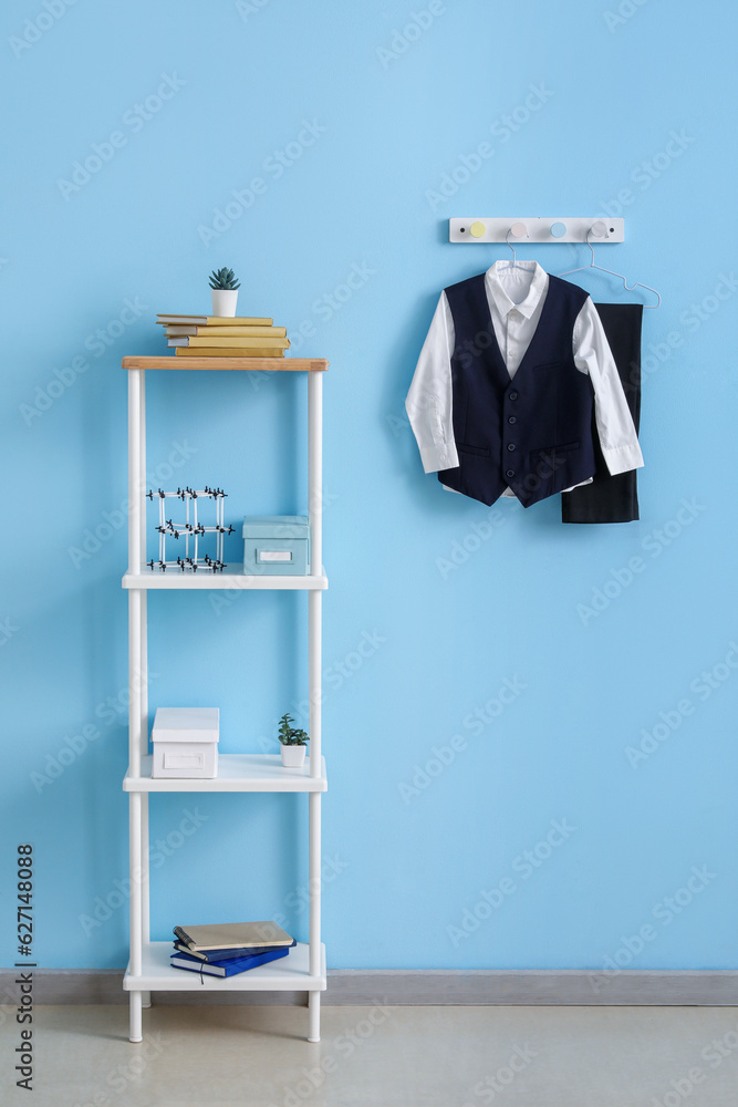 Shelving unit with books and stylish school uniform hanging on blue wall in room