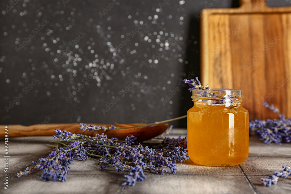 Jar of sweet lavender honey and flowers on grey tile table