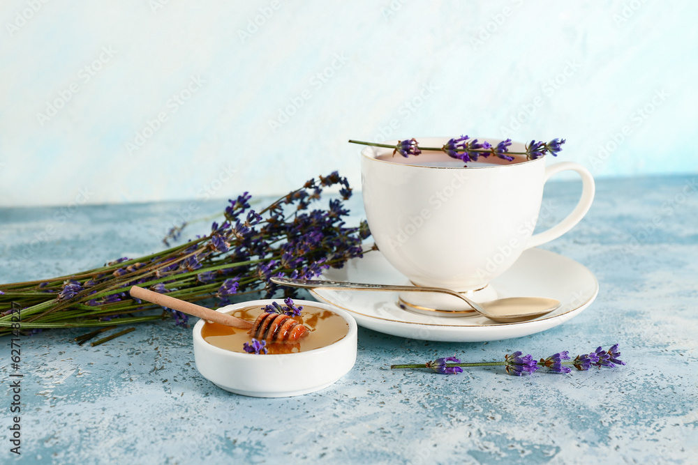 Bowl with sweet lavender honey and cup of tea on blue table