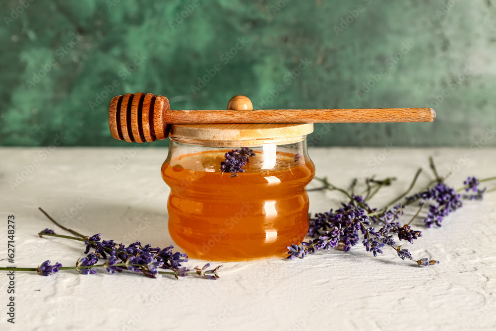 Jar of sweet lavender honey, dipper and flowers on white table