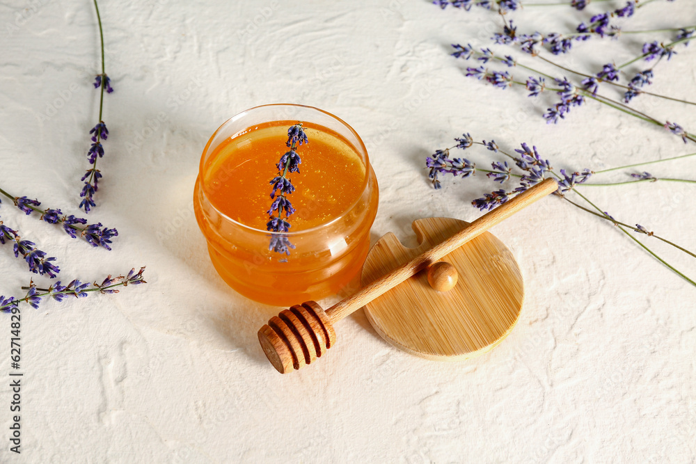 Jar of sweet lavender honey, dipper and flowers on white table