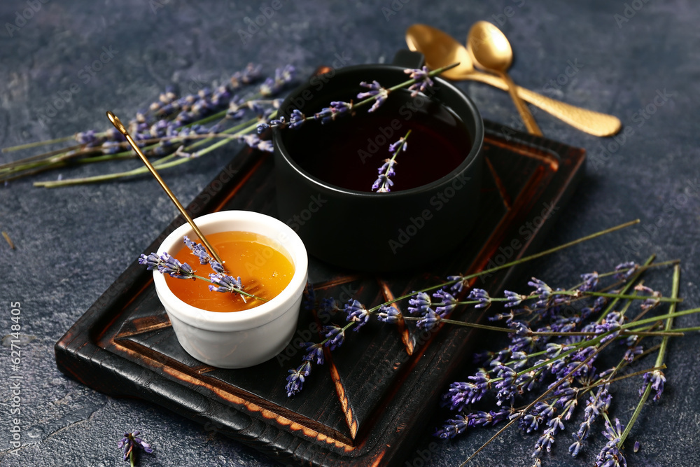 Bowl with sweet lavender honey and cup of tea on dark background