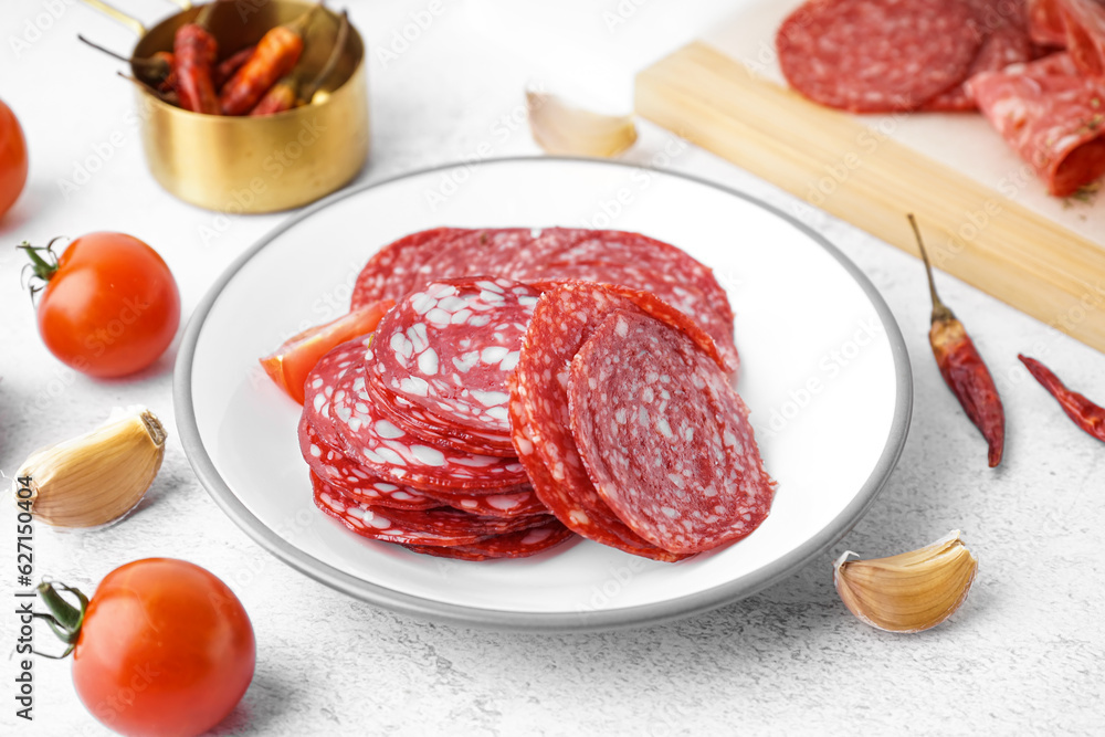 Plate with slices of tasty salami on light background