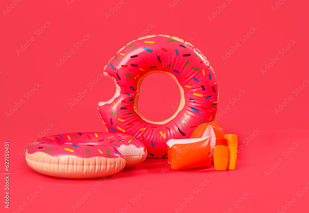 Inflatable rings in shape of donuts with beach accessories on red background