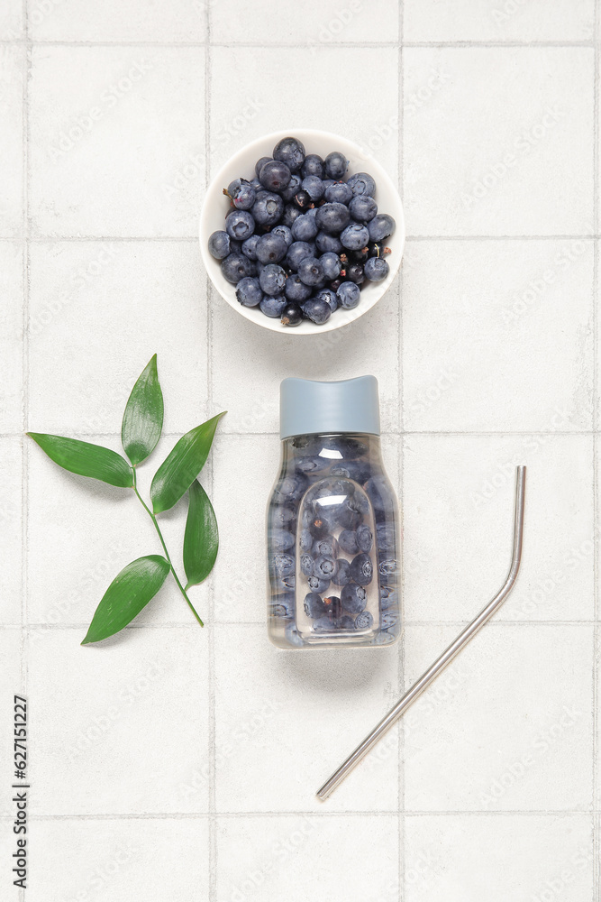 Sports bottle of infused water with blueberries and bowl of berries on white tile background